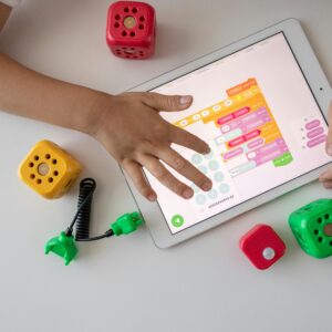 Child using digital tablet for coding education alongside colorful toy blocks.